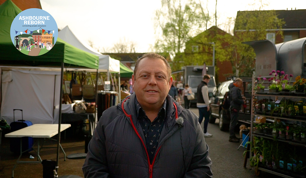 Sean Clayton stands in Shrovetide walk with Thursday Market flower stalls behind him